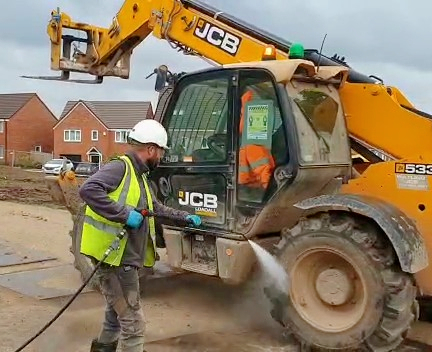 Image showing the our Brooklands Service Group trained operative cleaning the mud and debris off this JCB digger at a construction site 