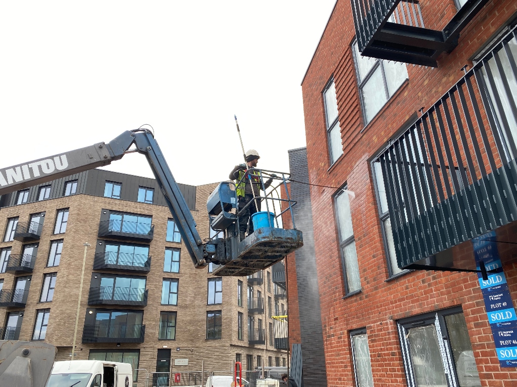An operative on a cherry picker carrying out an exterior cleaning service to clean bricks 