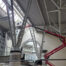 High-level industrial cleaning and maintenance work being carried out inside a modern building with steel beams and glass roof, using elevated work platforms and cherry pickers.