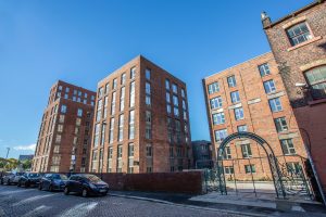 Modern brick residential buildings with large windows under a clear blue sky in Liverpool, showcasing professional building cleaning, painting, and on-site spraying services by Brooklands Group.