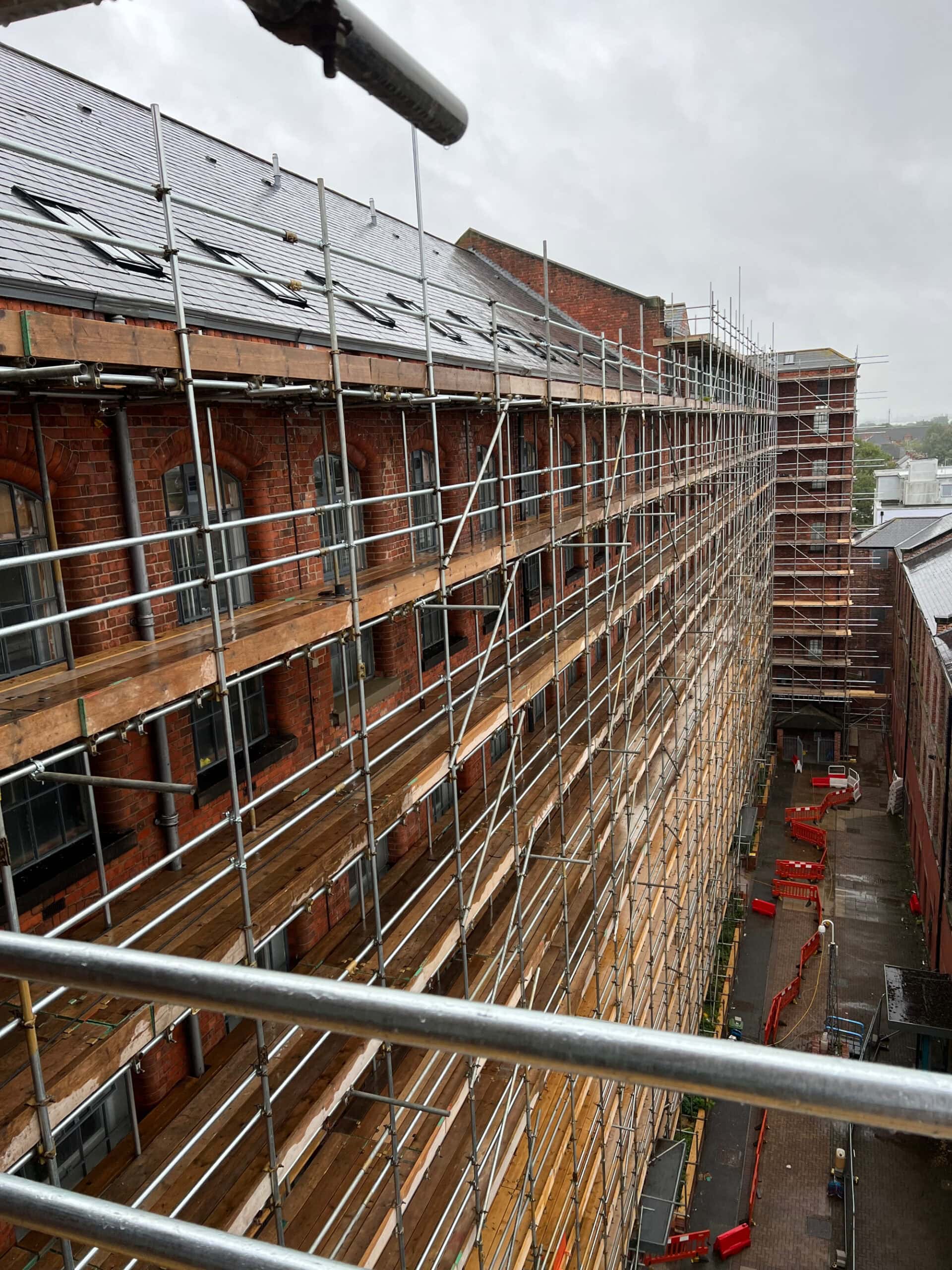 Brick Cleaning Services UK Scaffolding on a building exterior under renovation, providing safe access for brick cleaning work, with a cityscape view in the background.