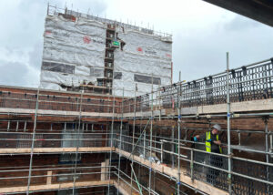 Multi storey commercial building with scaffolding surrounding it to acccess the bricks for brick cleaning technitian on high rise building under cloudy sky.