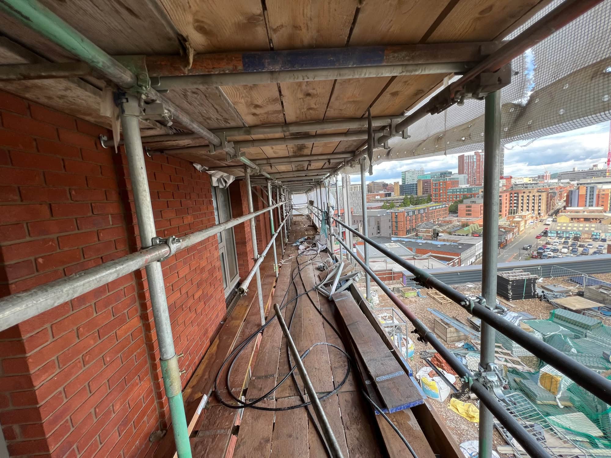 Exterior Brick Cleaning Services Scaffolding on a large high-rise commercial building exterior under renovation, providing safe access for exterior brick cleaning and brick cleaning work, with a view of Sheffield in the background.