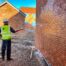 Man in high-visibility vest and helmet using pressure washer on brick walls.