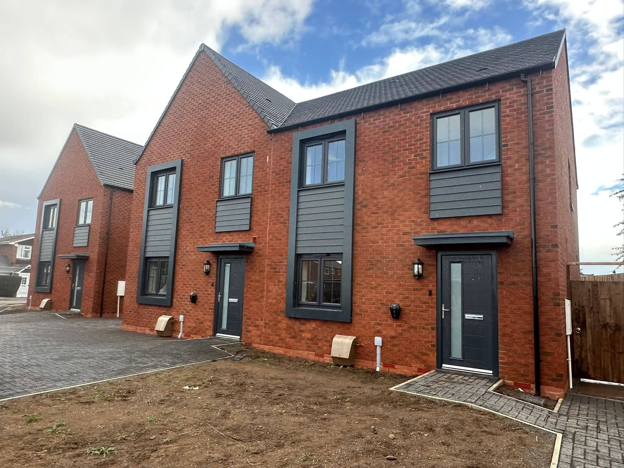 Modern red brick townhouse exterior with black framed windows and doors, featuring cladding accents and freshly paved pathways, showcasing professional brick cleaning of new bricks taken place to finish off the site.