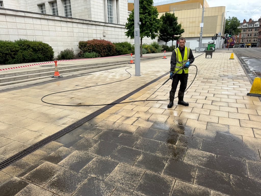 High-pressure cleaning worker jet washing pavement at a university building in Nottingham to remove oil spill, dirt and grime from paving.