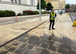 High-pressure cleaning worker jet washing pavement at a university building in Nottingham to remove oil spill, dirt and grime from paving.
