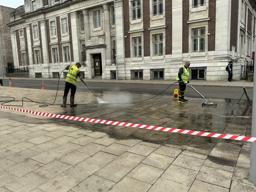 High-pressure cleaning of a city pavement with workers in high-visibility vests using pressure washers to remove dirt and grime from the surface. Removing Oil Spill off the paving.