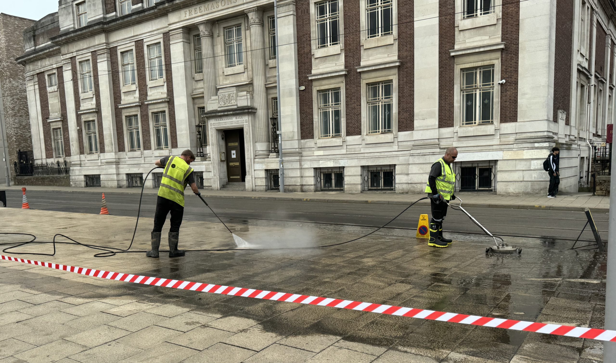 High-pressure cleaning of a city pavement with workers in high-visibility vests using pressure washers to remove dirt and grime from the surface. Removing Oil Spill off the paving.