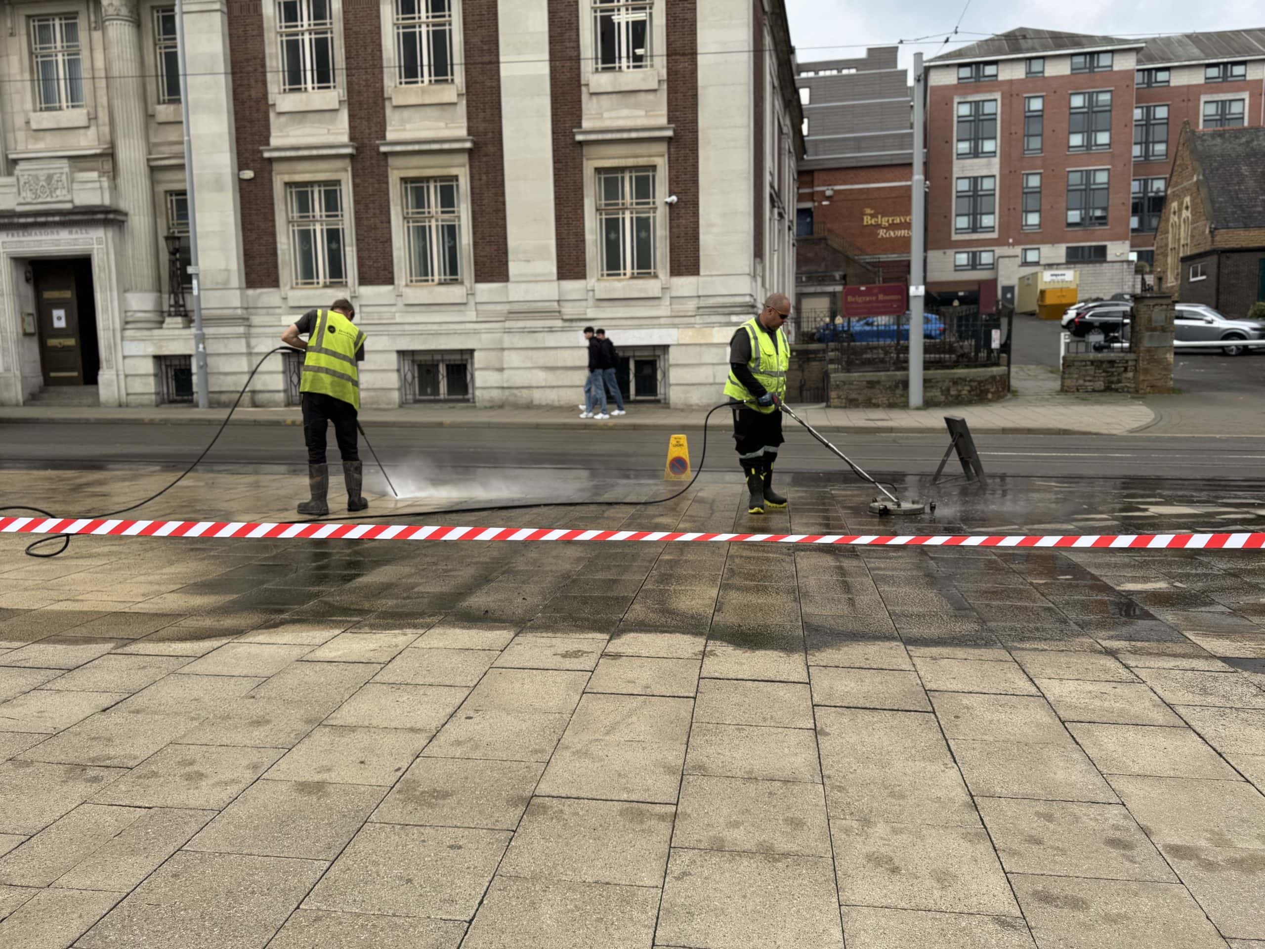 High-pressure street cleaning by workers in reflective vests removing dirt and grime from the pavement.