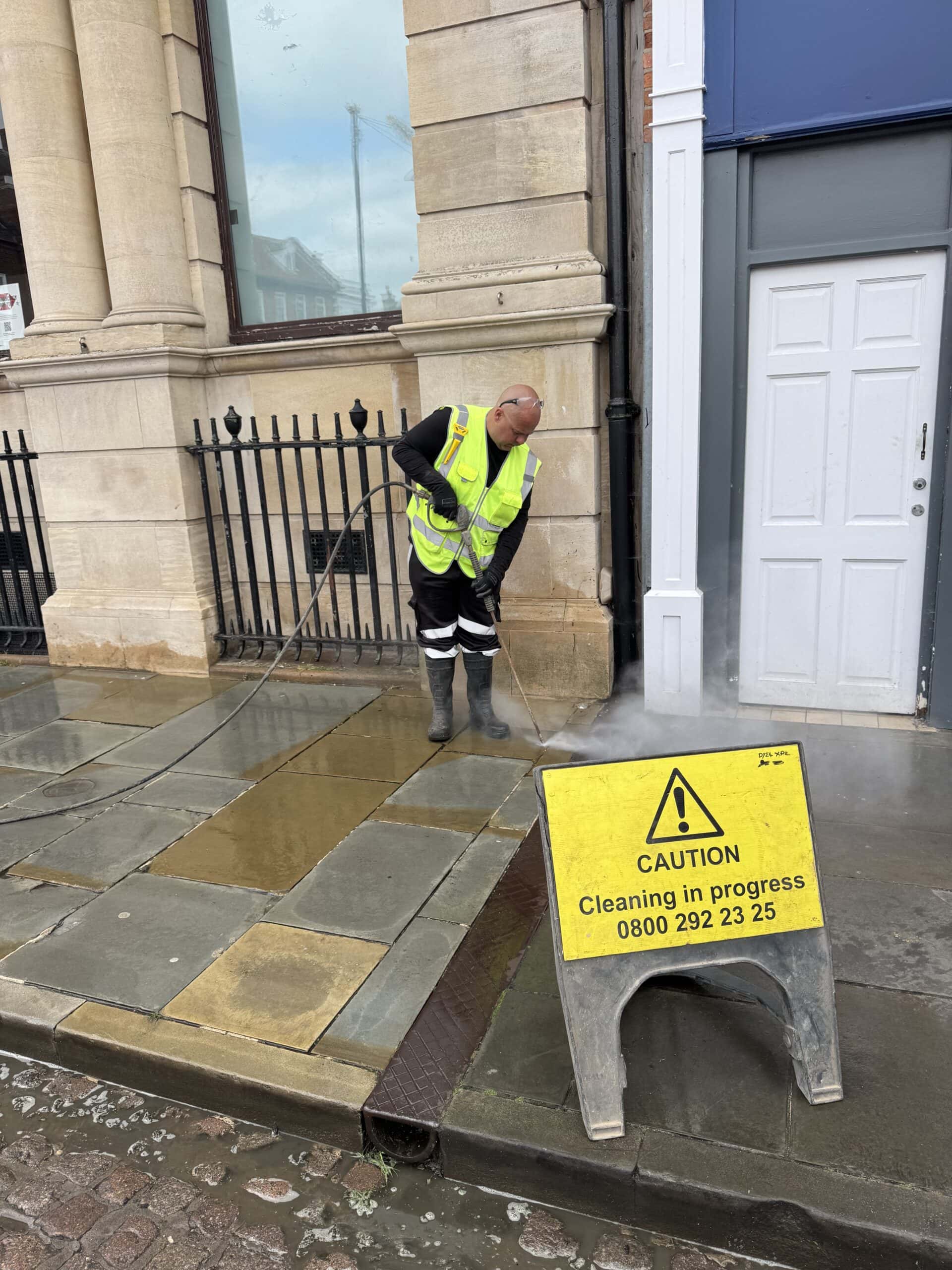 Steam cleaning of stone pavement on building exterior in progress.
