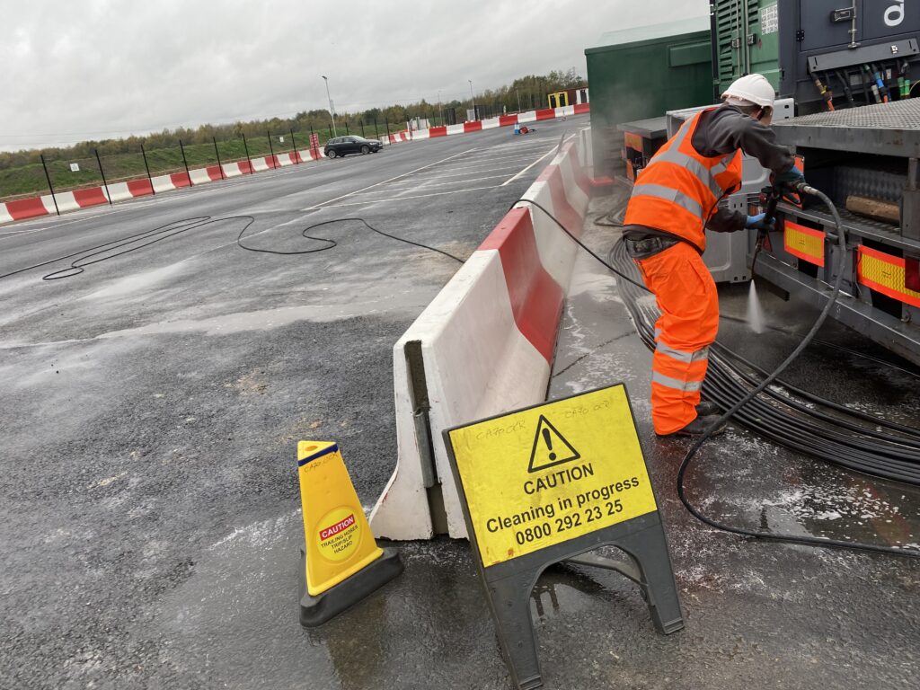 High-visibility worker cleaning tarmac surface to remove a sutance spillage