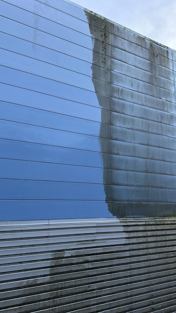 Modern industrial building with reflective metal panels and visible cleaning marks.