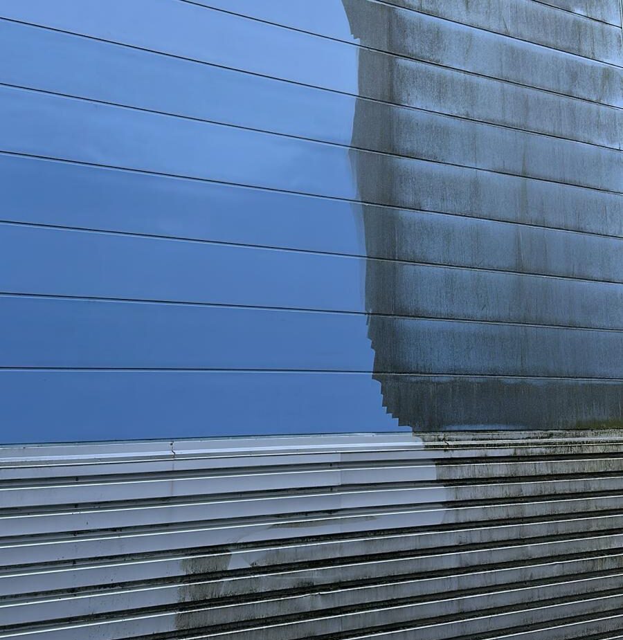 Showing the debris being removed by industrial cleaning services from industrial cladding. A clear line showing where the debris has been romvoed and the clean reflective metal panels and visible.
