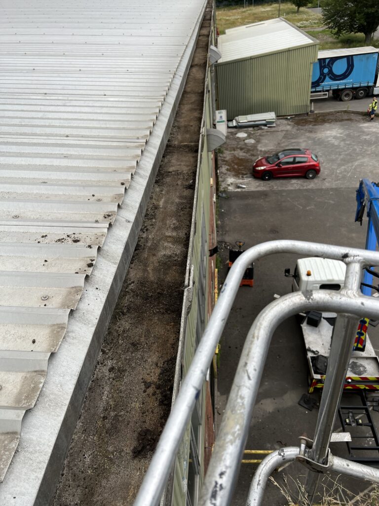Gutter cleaning with gloves and tools on an industrial building roof.
